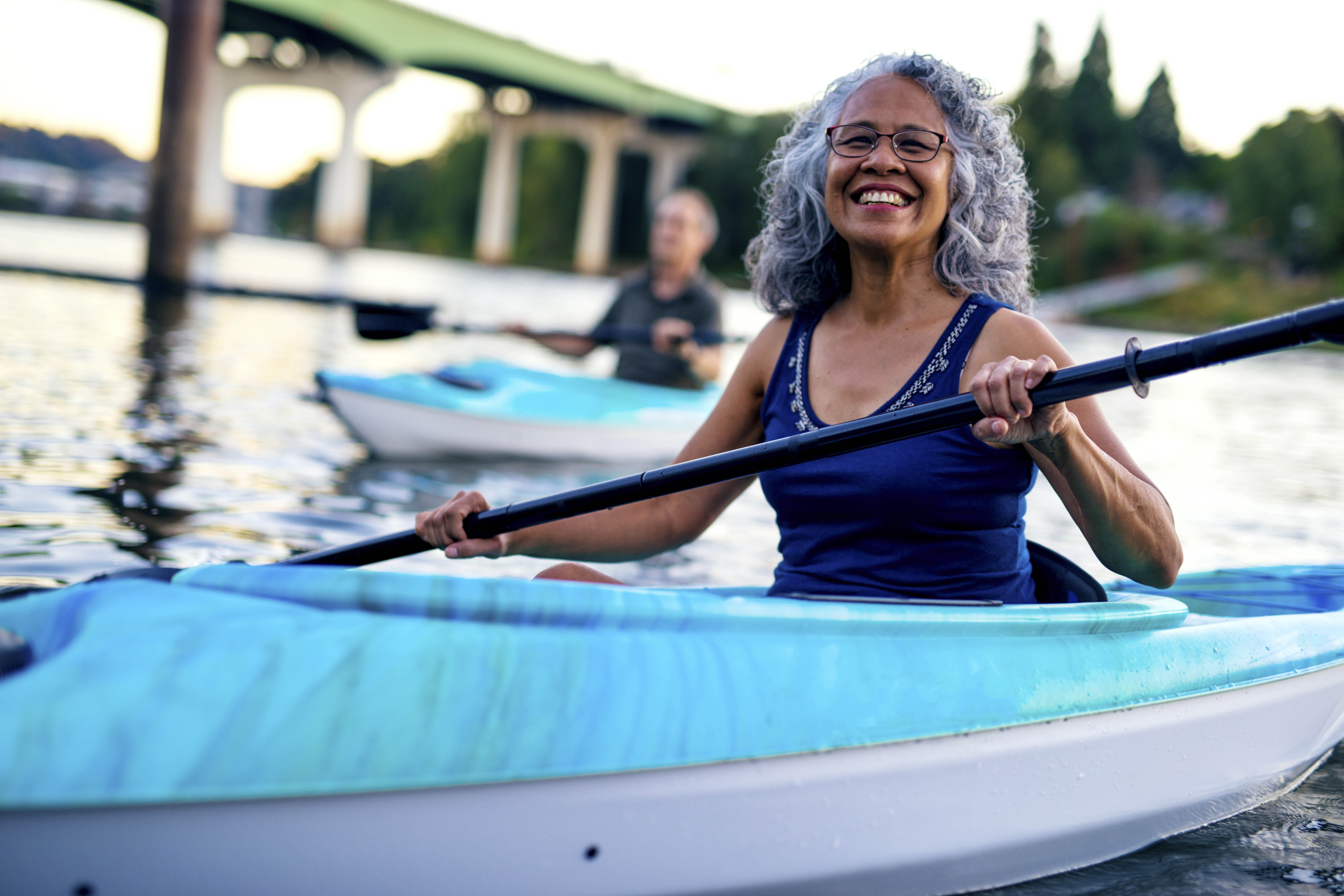mature woman kayaking on a river with man in the background